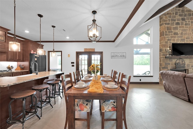 dining area featuring a stone fireplace, french doors, sink, ornamental molding, and a notable chandelier