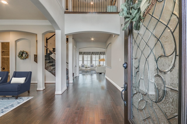 entryway featuring dark wood-type flooring, crown molding, and ornate columns