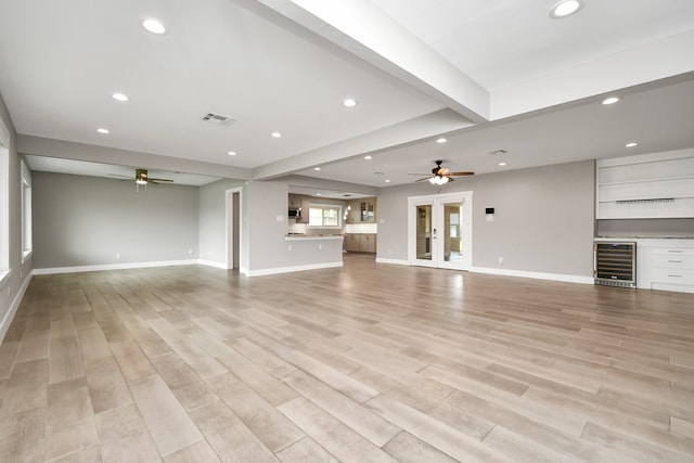 unfurnished living room featuring wine cooler, beam ceiling, ceiling fan, and light wood-type flooring