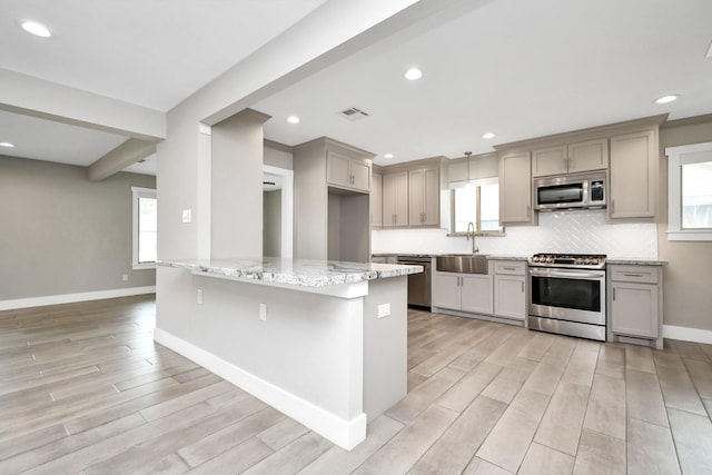 kitchen featuring gray cabinets, appliances with stainless steel finishes, sink, backsplash, and light stone counters