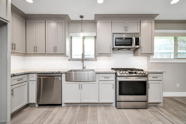 kitchen with hanging light fixtures, appliances with stainless steel finishes, sink, and light stone counters