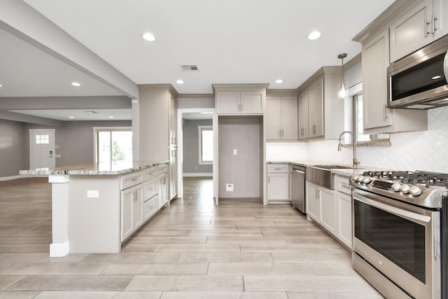 kitchen featuring sink, appliances with stainless steel finishes, hanging light fixtures, backsplash, and light stone counters