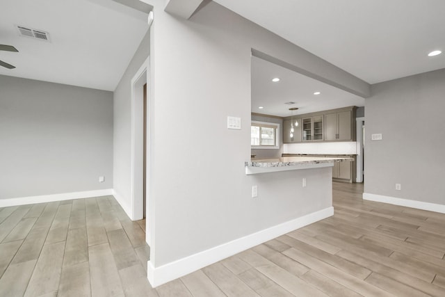 kitchen featuring a breakfast bar area, light stone counters, light hardwood / wood-style floors, and kitchen peninsula