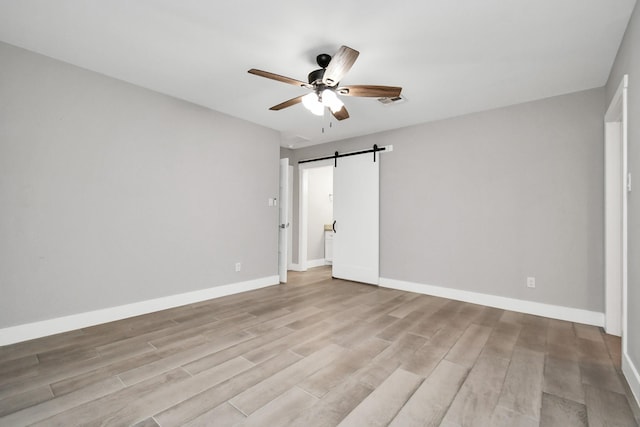 unfurnished bedroom featuring a barn door, ceiling fan, and light wood-type flooring