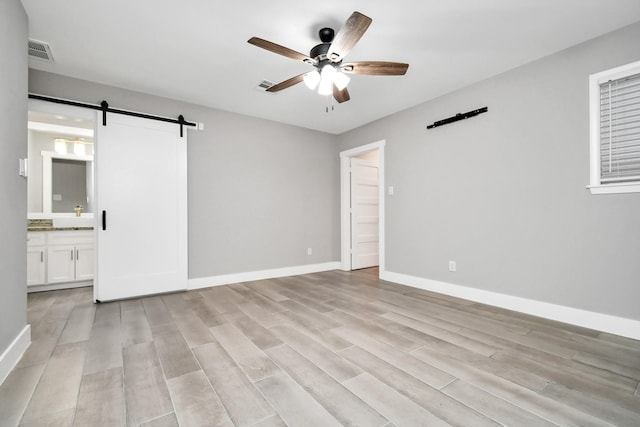 interior space with a barn door, light wood-type flooring, and ceiling fan