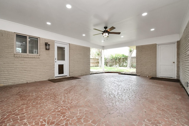 unfurnished living room with crown molding, ceiling fan, and brick wall