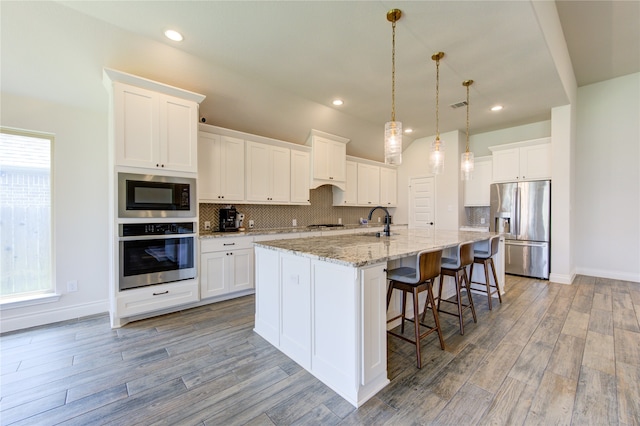 kitchen with appliances with stainless steel finishes, tasteful backsplash, wood-type flooring, and a healthy amount of sunlight