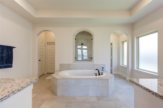 bathroom with a tray ceiling, a relaxing tiled tub, vanity, and tile patterned floors