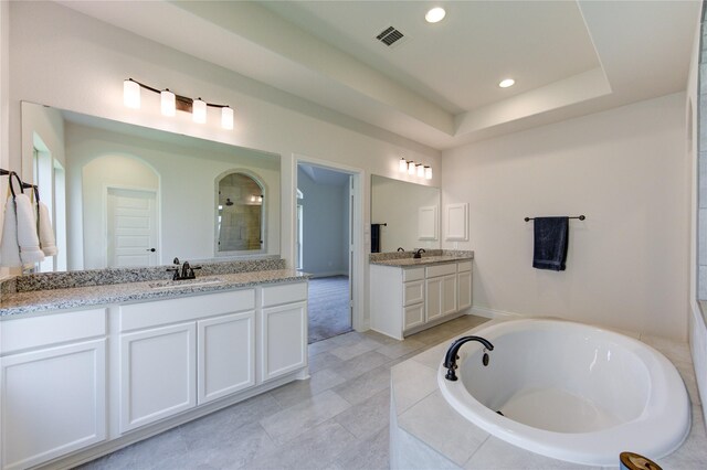 bathroom featuring tile patterned floors, a raised ceiling, dual bowl vanity, and tiled bath