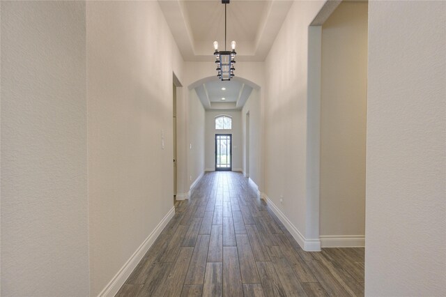 corridor featuring a notable chandelier, dark wood-type flooring, and a tray ceiling