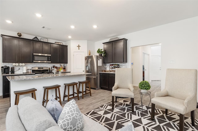 kitchen with stainless steel appliances, backsplash, a kitchen bar, a center island with sink, and dark brown cabinets