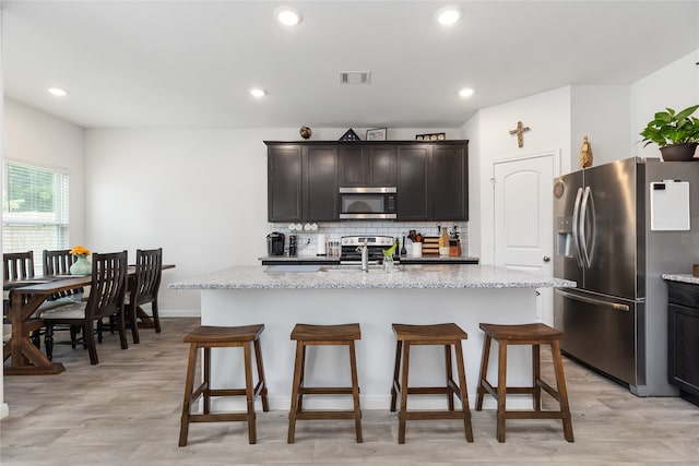 kitchen featuring a kitchen island with sink, light stone counters, and appliances with stainless steel finishes