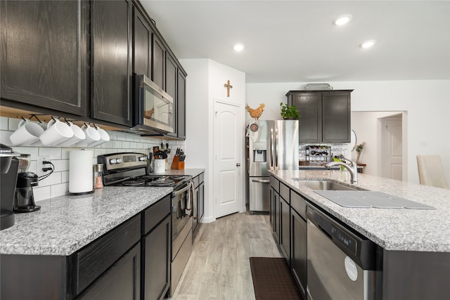 kitchen featuring dark brown cabinetry, stainless steel appliances, light hardwood / wood-style flooring, backsplash, and a center island with sink