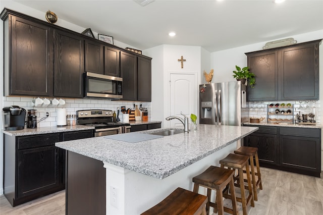 kitchen featuring light wood-type flooring, stainless steel appliances, backsplash, and an island with sink