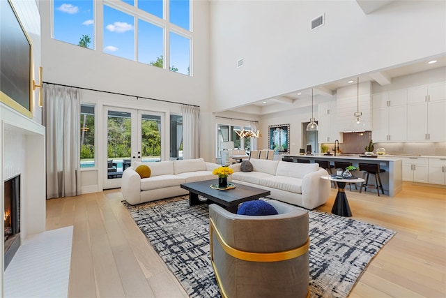 living room with light hardwood / wood-style floors, sink, french doors, and a towering ceiling