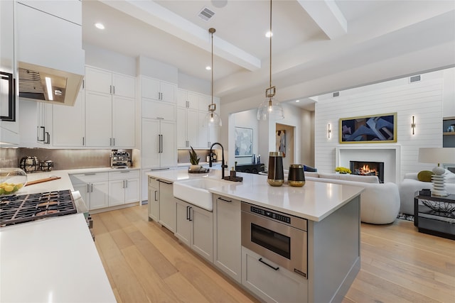 kitchen with premium range hood, a fireplace, light wood-type flooring, and a kitchen island with sink