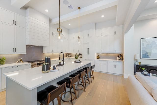 kitchen featuring backsplash, a center island with sink, light hardwood / wood-style flooring, high end stainless steel range, and a kitchen breakfast bar