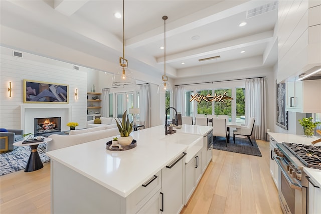 kitchen featuring light wood-type flooring, sink, a center island with sink, and high end range