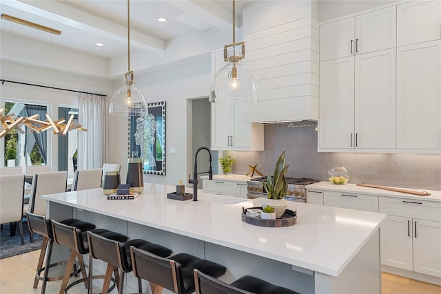 kitchen with decorative light fixtures, high end stove, beamed ceiling, a center island with sink, and light hardwood / wood-style floors