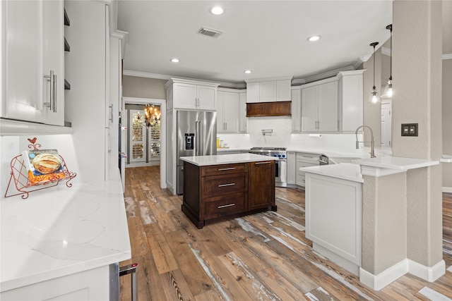 kitchen featuring light stone counters, high end appliances, kitchen peninsula, hardwood / wood-style floors, and ornamental molding