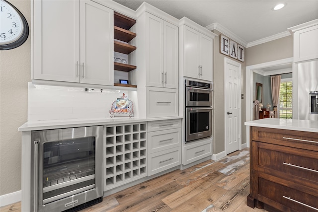 kitchen with white cabinets, beverage cooler, appliances with stainless steel finishes, and light hardwood / wood-style floors