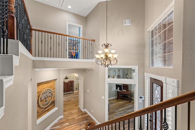 hall featuring an inviting chandelier, a towering ceiling, and hardwood / wood-style floors