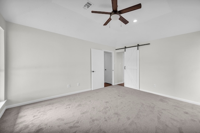 unfurnished bedroom with ceiling fan, a barn door, and carpet flooring