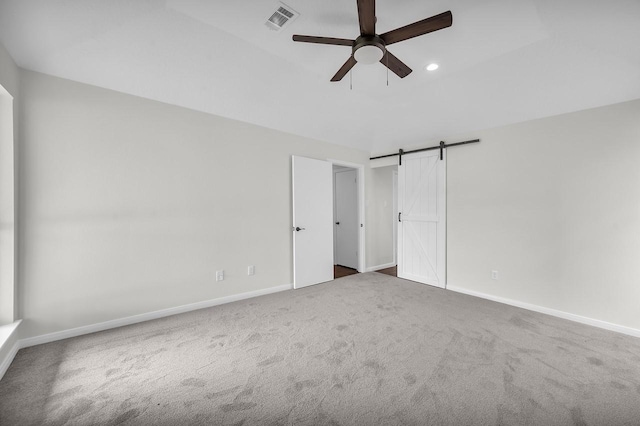 unfurnished room with visible vents, a ceiling fan, a barn door, carpet, and baseboards