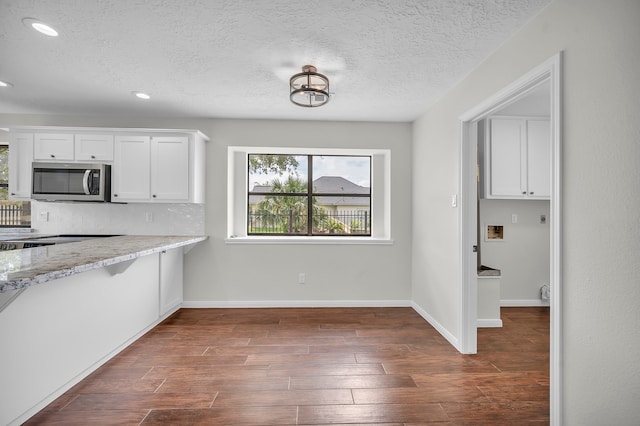 kitchen with dark wood-type flooring, light stone counters, tasteful backsplash, a textured ceiling, and white cabinetry