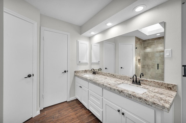 full bathroom with a skylight, a shower stall, wood finished floors, and a sink