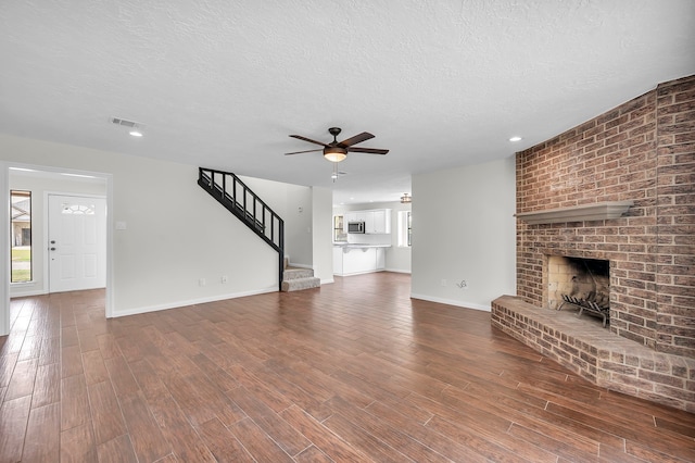 unfurnished living room featuring a brick fireplace, wood-type flooring, a textured ceiling, ceiling fan, and brick wall