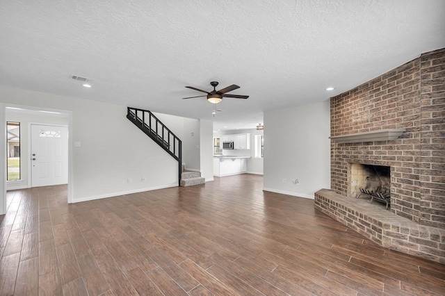 unfurnished living room with dark wood-type flooring, a ceiling fan, a textured ceiling, stairway, and a fireplace