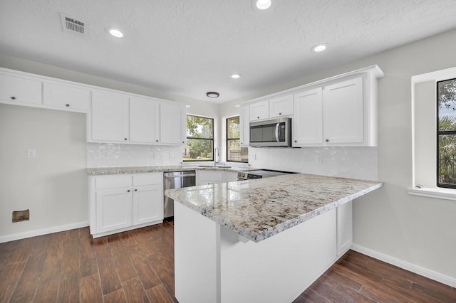 kitchen featuring appliances with stainless steel finishes, a peninsula, dark wood-style flooring, and white cabinetry