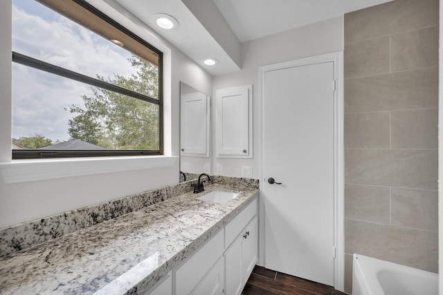 bathroom with vanity, a bath, wood finished floors, and recessed lighting