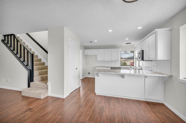 kitchen with hardwood / wood-style floors, light stone counters, a textured ceiling, white cabinetry, and kitchen peninsula