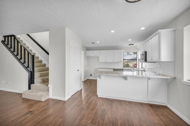 kitchen with light stone countertops, appliances with stainless steel finishes, a peninsula, white cabinetry, and dark wood-style flooring