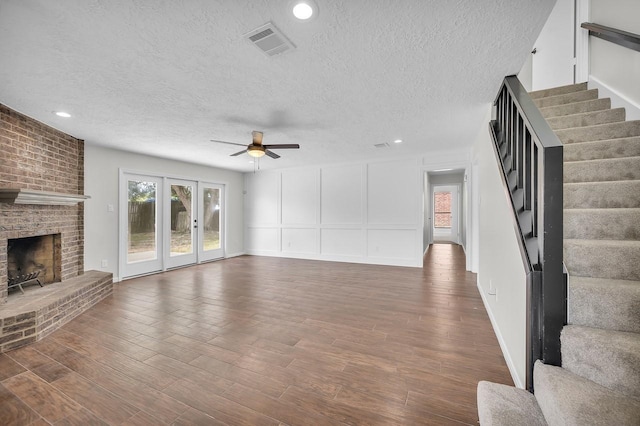 unfurnished living room featuring stairway, a decorative wall, wood finished floors, and visible vents