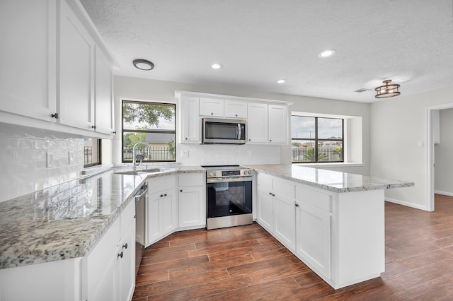 kitchen featuring appliances with stainless steel finishes, decorative backsplash, light stone counters, white cabinetry, and kitchen peninsula