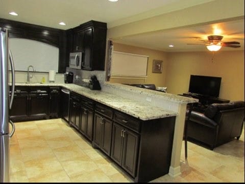 kitchen with light tile patterned flooring, stainless steel refrigerator, light stone counters, ceiling fan, and sink