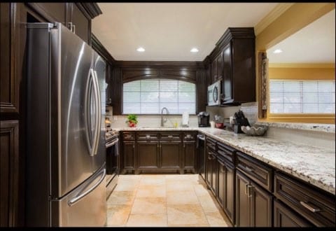 kitchen with light tile patterned floors, light stone countertops, appliances with stainless steel finishes, dark brown cabinetry, and sink