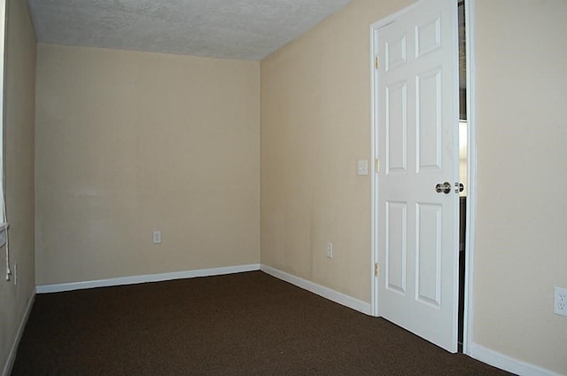 spare room featuring dark colored carpet and a textured ceiling