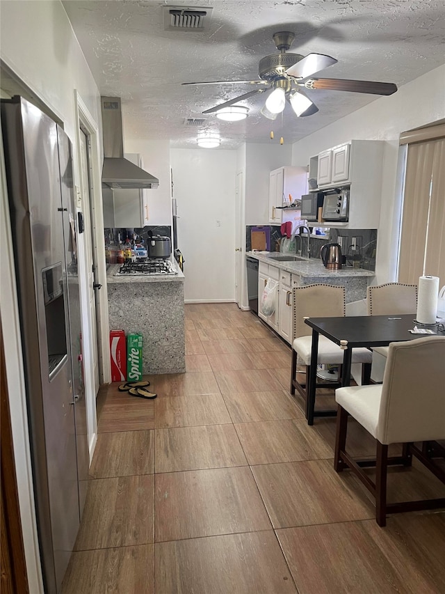 kitchen with appliances with stainless steel finishes, wall chimney range hood, sink, a textured ceiling, and ceiling fan