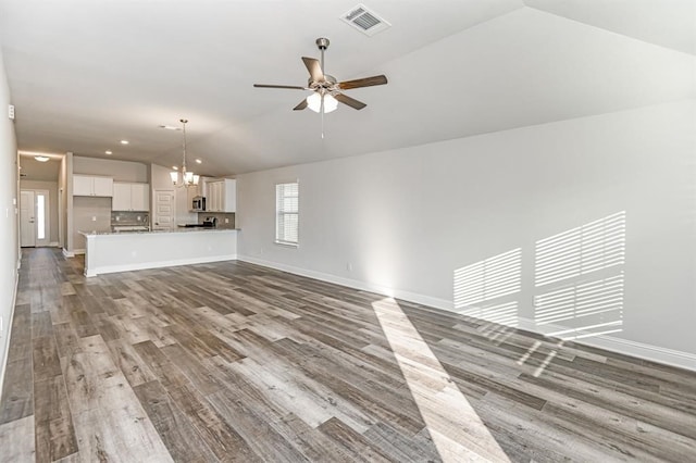 unfurnished living room with ceiling fan with notable chandelier, light hardwood / wood-style floors, and vaulted ceiling