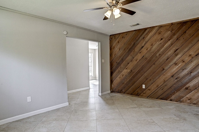 tiled spare room with wood walls, a textured ceiling, and ceiling fan