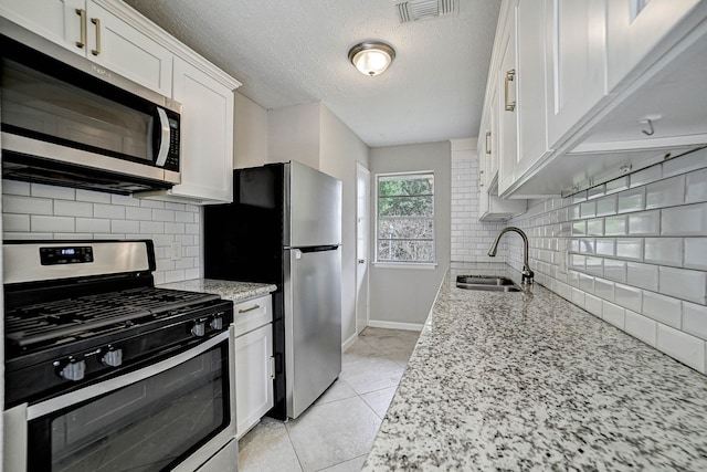 kitchen featuring white cabinetry, backsplash, light stone counters, stainless steel appliances, and sink