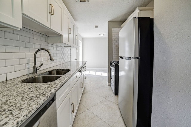 kitchen featuring a textured ceiling, light stone counters, stainless steel appliances, decorative backsplash, and sink