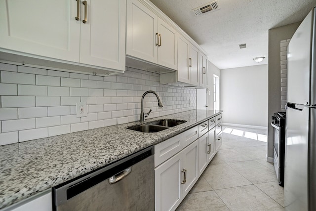 kitchen featuring white cabinets, decorative backsplash, light stone countertops, appliances with stainless steel finishes, and a textured ceiling