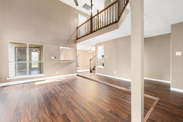 unfurnished living room featuring a towering ceiling, dark hardwood / wood-style flooring, and an inviting chandelier