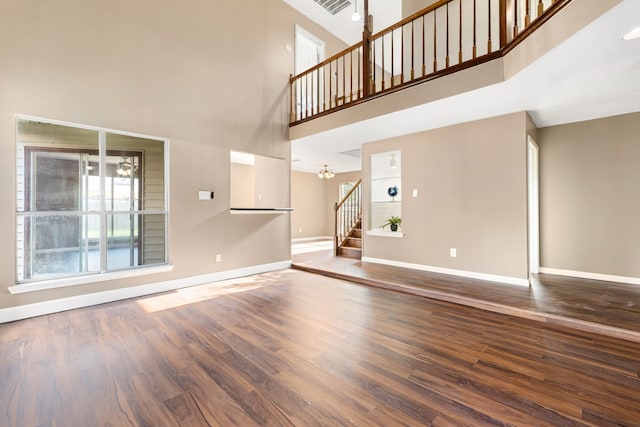 unfurnished living room featuring dark wood finished floors, a high ceiling, a chandelier, baseboards, and stairs