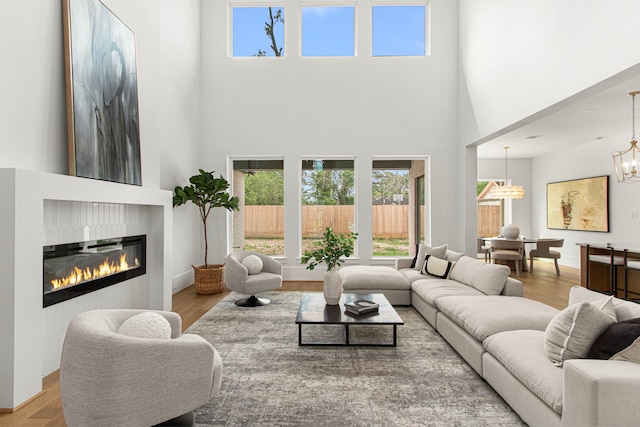 living room with a chandelier, wood finished floors, baseboards, and a glass covered fireplace